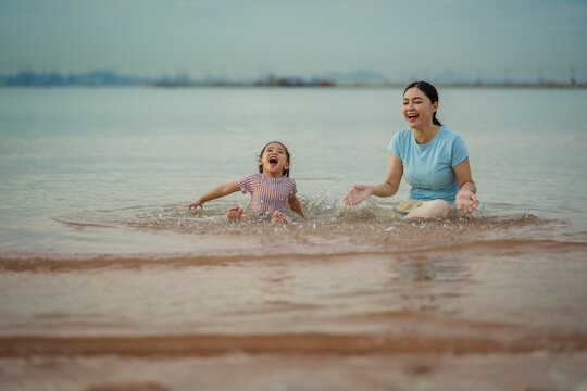 happy preschool child girl playing water splashing with her mother on sea beach in Pattaya, Thailand