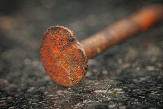 Macro close up shot of an old weathered rusty metal nail head resting on a dark gritty textured surface background