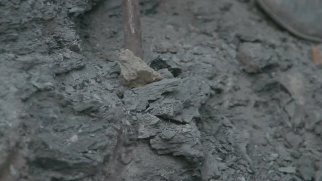 Cinematic close-up shot of a craftsman drilling and working on a hard rock and soil layer at an excavation or mining site.