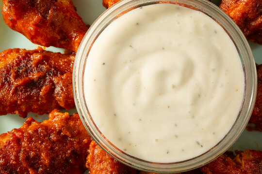 A top down view of a bowl of gluten-free, dairy-free ranch dressing, with some Buffalo wings.