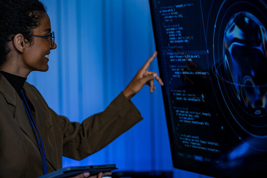 A female developer reviews software output on a glowing display during a focused late-night session at her desk, in an advanced, screen-filled operations center.