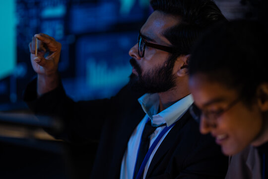 A team of engineers examines a white robotic prosthetic arm laid across a workstation in a blue-lit laboratory, during a productive late shift in the dark office.