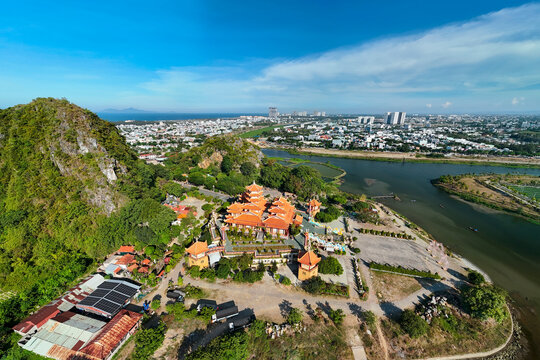Aerial view of the large Buddhist temple surrounded by green hills near the river in Da Nang Vietnam under the bright afternoon sun