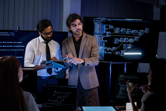 A night-shift team monitors systems across rows of screens in a blue-lit operations room late into the evening, as the diverse team works through the night in a quiet, modern blue-lit.