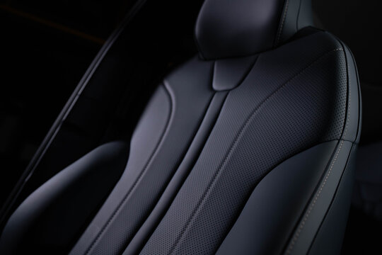 Close‑up of car seat backrest and headrest upholstered in dark perforated leather with visible stitching. Lighting emphasizes contours, ergonomic shape, and premium craftsmanship. 