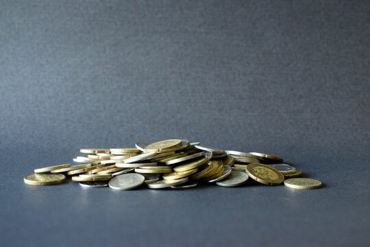 A wide horizontal shot featuring a shallow pile of mixed gold and silver coins centered on a plain dark backdrop, highlighting general financial concepts, fiscal policy or debt management.