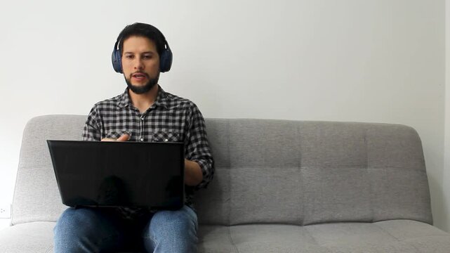 A Latin man sitting on a grey couch in a video meeting job on a remote working concept