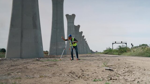 Survey engineer using an automatic level mounted on a tripod to perform elevation measurements during construction of an elevated railway infrastructure project.
