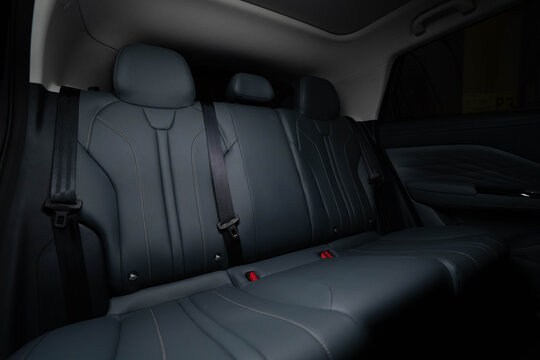 Rear seat interior of modern car featuring three dark leather seats with stitching, headrests, and seat belts. Lighting highlights contours and premium craftsmanship, emphasizing comfort, durability, 