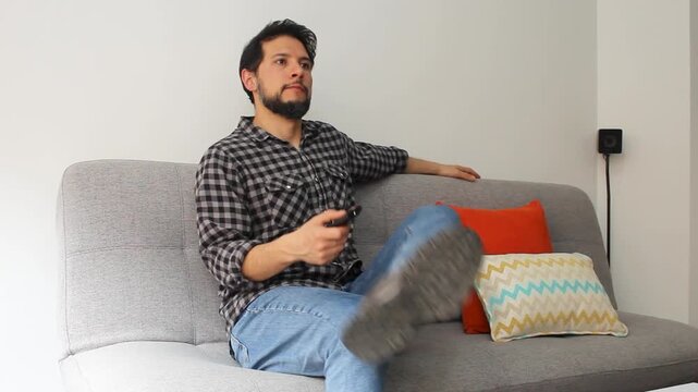 A hispanic man sitting down in a couch and turning on a smart tv with a remote controller