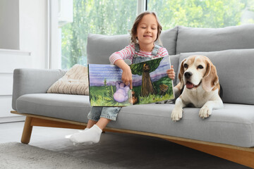 Obraz premium Cute little girl with Beagle dog and book on sofa in living room