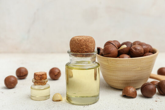 Bottles of macadamia oil and bowl with nuts on grunge table, closeup