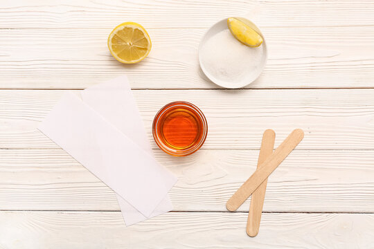 Glass bowl with sugaring paste, wax strips and sticks on white wooden background