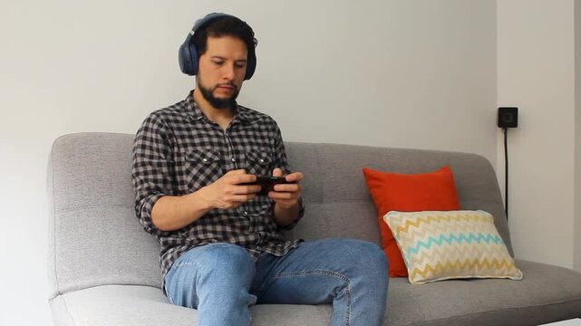 Detailed view of a caucasic man sitting on a couch playing games on his smartphone and using a wireless headset