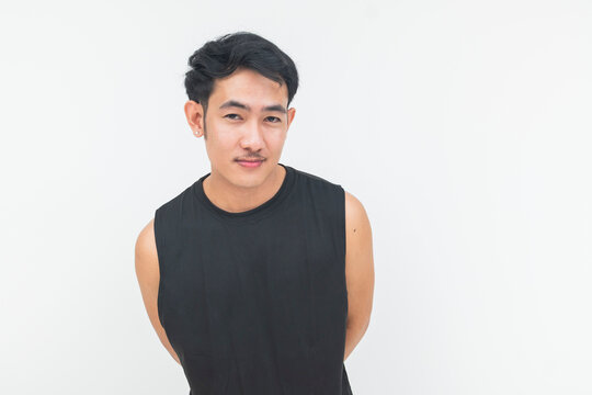 A young Southeast Asian man in a black athletic tank top gives a slight smile while standing and leaning slight with his hands behind his back.