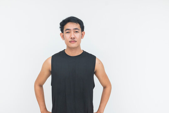 A young Southeast Asian man in a black athletic tank top stands confidently with his hands on his waist in a studio.