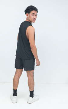 A young Southeast Asian man in athletic wear looks back over his shoulder with a confident expression while standing in a studio.