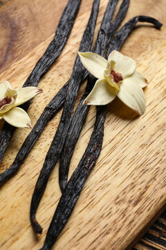 Wooden board with aromatic vanilla sticks and flowers, closeup