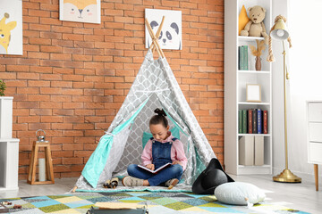 Obraz premium Cute little girl reading adventure book in play tent at home