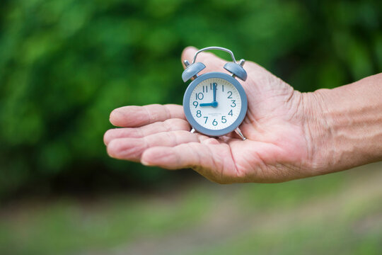 Alarm clock in the hand of a man on nature background.