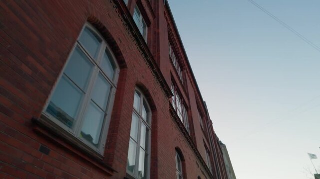 Red brick facade sunset windows, gimbal stabilizer shot. 60fps tracking view walking on sidewalk looking up at building architecture in Copenhagen Denmark.