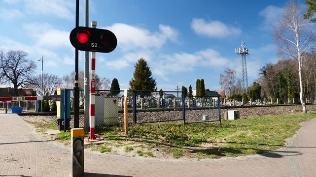 A peaceful Polish level crossing beside the historic Jastarnia cemetery. Modern safety barriers and lights frame the scenic Hel Peninsula tracks.