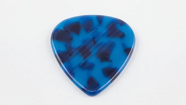 Blue tortoise shell guitar pick isolated on white background with resting white surface entertainment