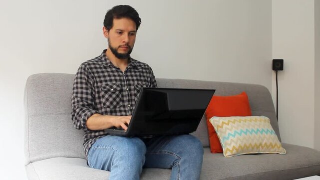 Detailed view of a man sitting on a couch typing on a laptop over his legs in a home office concept