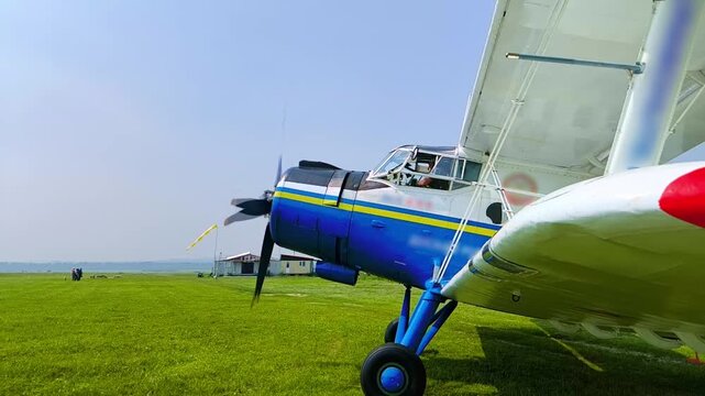 An-2 aircraft with a rotating propeller before taking off at a dirt airfield. Side view of a classic biplane during flight preparation.
