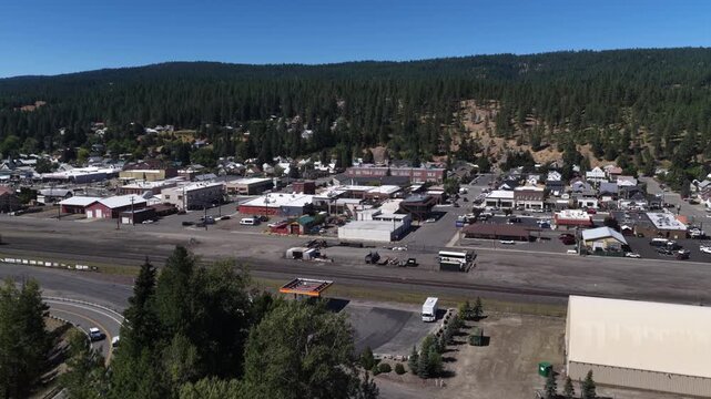 Aerial of small town center and railroad tracks in Cle Elum Washington with extensive commercial buildings and forest