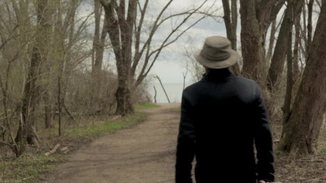 Senior man pulls gear cart along tree-lined trail toward Lake Ontario at Lynde Shores Conservation Area, Whitby, Ontario, Canada.