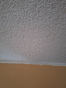 Textured popcorn ceiling with a visible crack running down to a tan wall