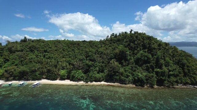 An isolated, uninhabited tropical island with a beach of crystal clear waters and white sand seen from afar. Palm trees and untouchable local flora. Filmed with a Drone in Palawan, Philippines, Asia.