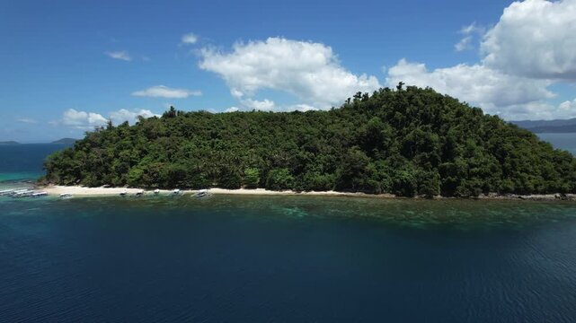 An isolated, uninhabited tropical island with a beach of crystal clear waters and white sand seen from afar. Palm trees and untouchable local flora. Filmed with a Drone in Palawan, Philippines, Asia.
