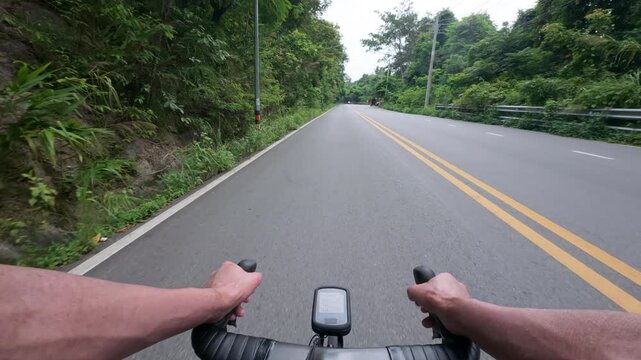 First-person POV footage of a road cyclist descending an empty winding mountain road surrounded by lush tropical forest. Smooth asphalt, sweeping curves, and immersive riding perspective create a clea