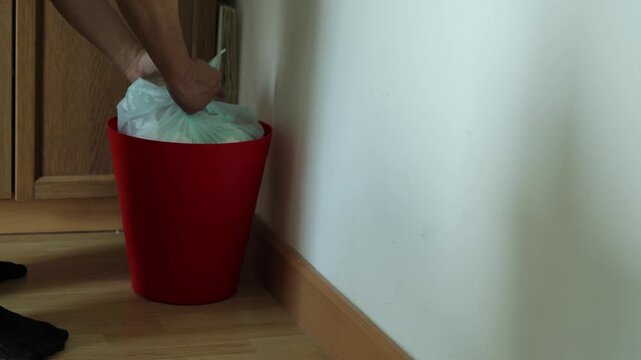 Horizontal 4K video of a man tying the plastic trash bag inside a red bin near the wall and carrying the garbage package away