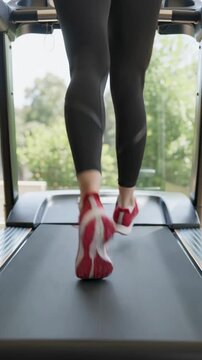 Close-up of legs running on treadmill in gym, vertical shot