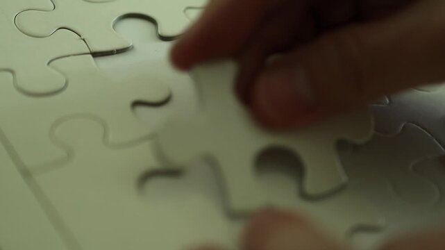 Horizontal 4K close up video of male hands trying to fit various blank white jigsaw puzzle pieces into empty gaps without success