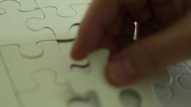 Horizontal 4K close up angle of a man attempting to assemble unmatched white jigsaw puzzle pieces into different empty spots