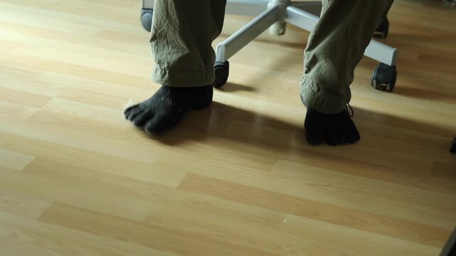 Horizontal 4K low angle shot of a man sitting on an office chair tapping his feet in socks on parquet floor to music rhythm