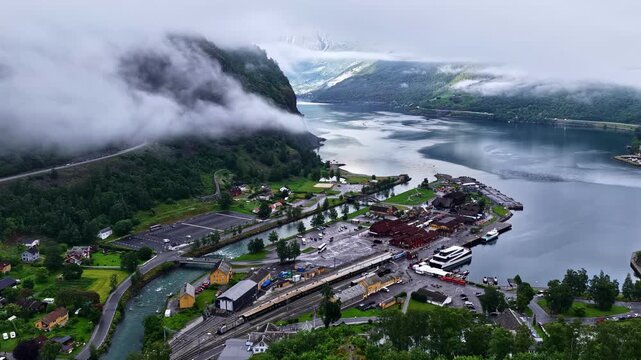 Time lapse shows clouds drifting over mountains above Flam village with train cars and boat docked