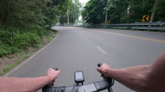 First-person point of view of a road cyclist riding through a sweeping mountain curve surrounded by lush tropical forest. The immersive footage captures endurance cycling, scenic mountain roads, outdo