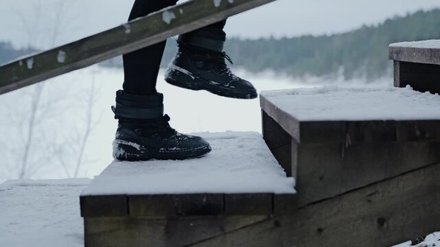 Slow motion close up of black winter boots climbing snowy wooden stairs in Ogre Blue hills