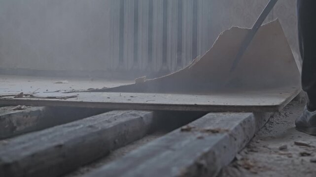 Dust rises as worker pries worn wooden flooring during slow renovation
