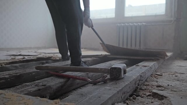 Low angle reveals heavy tools as worker lifts damaged flooring through dusty air
