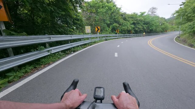 First-person POV footage of a road cyclist climbing a quiet mountain road surrounded by lush tropical forest. The smooth asphalt, roadside guardrail, and gentle uphill curve create an immersive endura