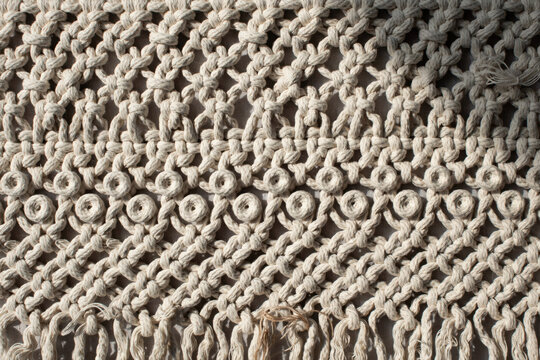 Close up of intricate handmade macrame textile wall hanging with woven cotton rope featuring repetitive knot patterns and dangling fringe ends
