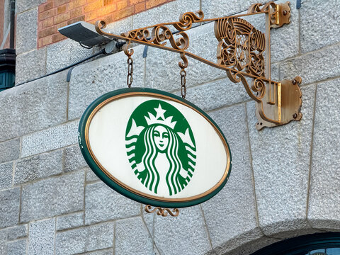 Quebec City, Quebec, Canada. July 21, 2026. Low angle view of an oval vintage Starbucks coffee logo sign hanging on a stone wall exterior.