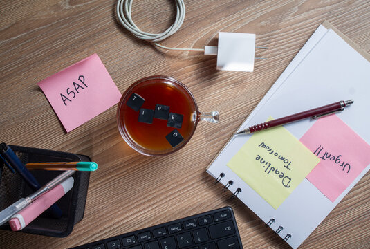 Burnout overworked and tired office worker. A coffee cup with keyboard keys forming tired surrounded by urgent office sticky notes. Employee burnout and work overload concept