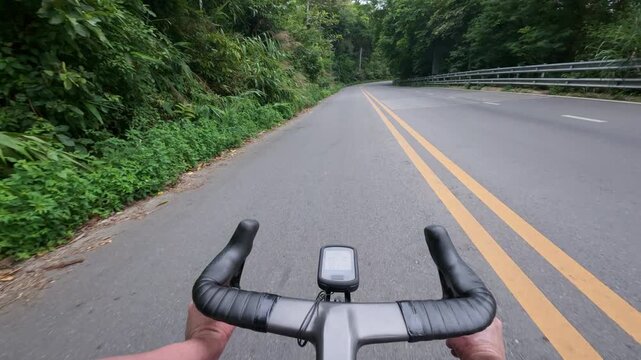 First-person POV footage of a road cyclist descending a smooth winding mountain road surrounded by lush tropical forest. Clean asphalt, sweeping curves, and immersive riding perspective create a dynam